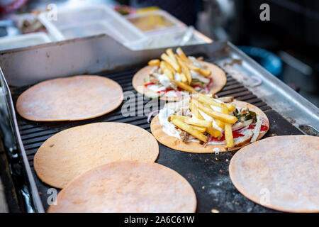 Fast food on the street. A delicious dish of meat and sauce with potatoes and vegetables on a bread cake. General form. Stock Photo