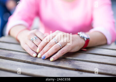 Close up of free female hands with manicure and accessories lie one on the other on the brown wooden table. Stock Photo