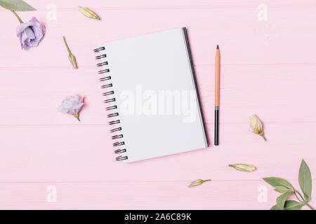 Empty open notebook and pencil among fresh lisianthus flowers and green leaves on pink background, top view. Stock Photo
