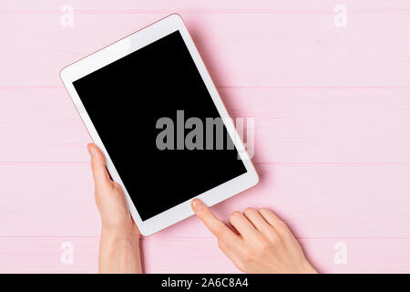 Mockup image of woman hands holding tablet pc with blank screen on pink desktop, top view. Stock Photo