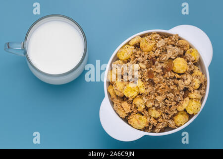A mixture of cereals dried and nuts with milk at breakfast. Glass cup of milk with rolled oats in a white plate on blue table. White bowl of granola w Stock Photo