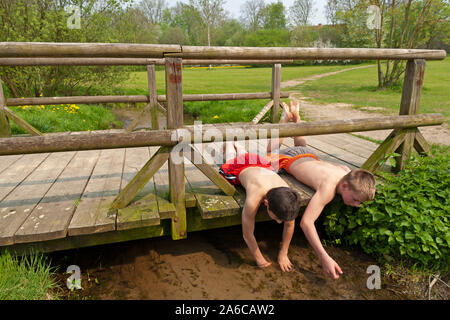 Two boys are lying on a wooden bridge playing in a stream. Stock Photo