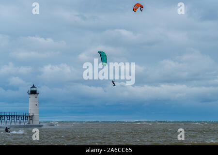 A kite surfer flies high in front of the Manistee North Pierhead Lighthouse in Michigan, USA with another kite surfer is on the surface of the water. Stock Photo