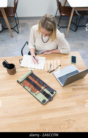 A woman sits at a table in a cafe making notes and sketching in a notepad Stock Photo