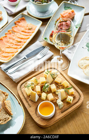 Cheese plate. Focus on delicious cheese mix with walnuts, honey on wooden table. Various snacks and antipasti on the table. Restaurant menu. Stock Photo
