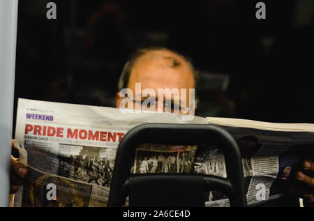 Middle age man very focused is reading a newspaper in the underground train. Headlines of the article is 'Pride Moment' Stock Photo
