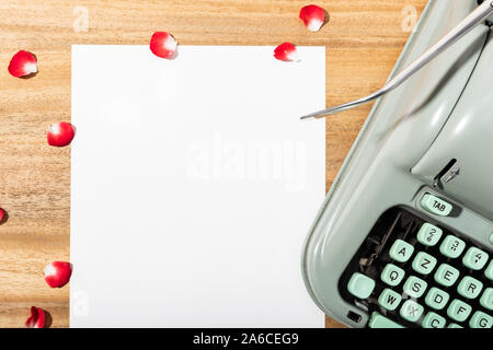 Love letter. Desk with blank paper, retro typewriter and red rose petals. Love concept Stock Photo