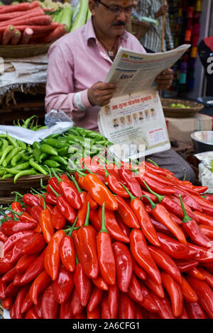 Red and green chilis on sale at a market in Mumbai, India, the vendor engrossed in his newspaper Stock Photo