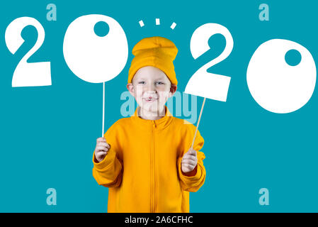 cheerful boy in a yellow hat and jacket holding the figures 2020 on a bright colored background Stock Photo