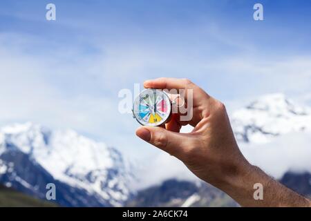 Magnetic compass. Hand holding a compass against a blue sky. The compass has a free-swinging magnetised needle, which is seen pointing to North on the dial. The dial is graduated in degrees and shows the cardinal points: north (N), south (S), east (E) and west (W). The needle aligns itself with local lines of magnetic force to indicate the direction of the north (shown by the yellow tip) and south magnetic poles. Stock Photo