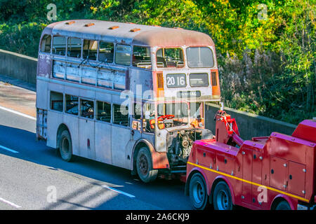 1950s-era automobiles barn garage find vehicle restoration project; Vintage bus towed on car trailer for restoration. UK Vehicular traffic derelict condition, rare collectible vintage classic transport, vintage, old buses, classics north-bound on the 3 lane M6 Motorway highway. Stock Photo