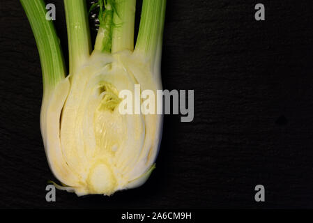 A sliced half fennel tuber lies on a black plate of slate with text box Stock Photo