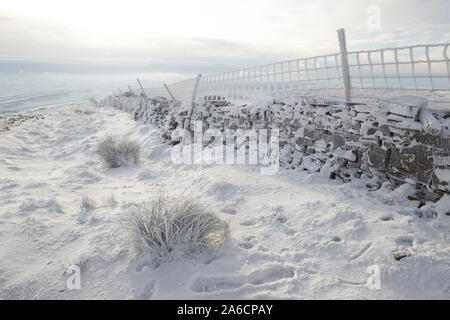 Dry stone wall and wire fence covered in hoar frost on Whernside carpeted in snow and ice mid winter Yorkshire Dales Stock Photo