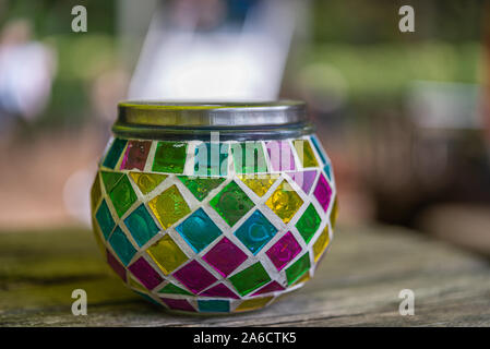 multicolor glass candle stand with a metal lid on a wooden table against a blurry background Stock Photo