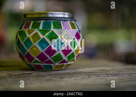 multicolor glass candle stand with a metal lid on a wooden table against a blurry background Stock Photo