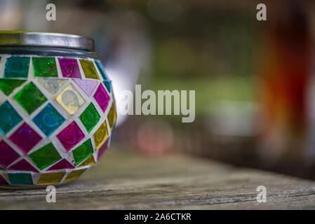multicolor glass candle stand with a metal lid on a wooden table against a blurry background Stock Photo