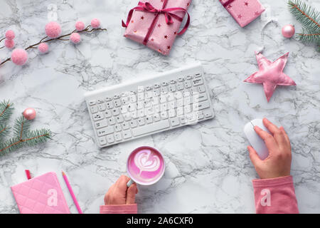 Christmas flat lay on marble table, festive workspace with computer keyboard. Hands holding mouse and cup of beetroot latte. Winter decorations: fir t Stock Photo