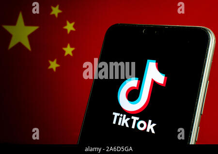 TikTok app logo on the screen and flag of China on a blurred dark background. Stock Photo