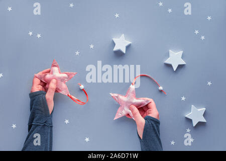 Creative Christmas flat lay in pastel colors on silver grey paper background. Hands holding soft textile stars, gray background with large and small p Stock Photo