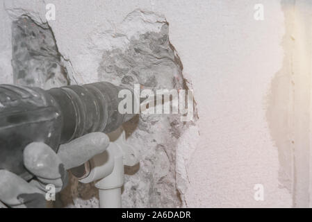 Hammer Drill in the hand in glove drills concrete wall with lens flare. Selective focus. Stock Photo