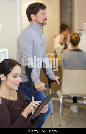 woman with tablet man in cruches in waiting room Stock Photo