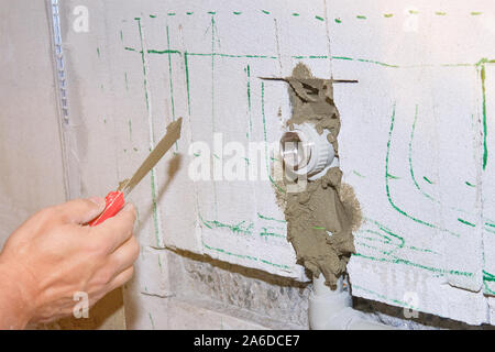 Builder holds a spatula in his hand and covered with cement mortar hole with pipe in the wall with lens flare. Stock Photo