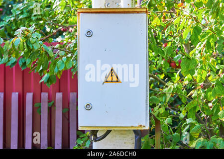 Locked rusty grey electric panel with hazard sign on the grey concrete pillar Stock Photo