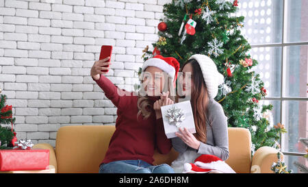 Asian women smiling and showing gift, taking a selfie by mobile smartphone in Christmas holiday Stock Photo