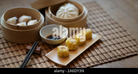 Chinese steamed dumpling and steamed pork bun in a bamboo steamer with chopstick on wooden table with copy space Stock Photo