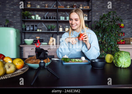 Young beautiful blonde takes on videos as she cooks in the kitchen Stock Photo