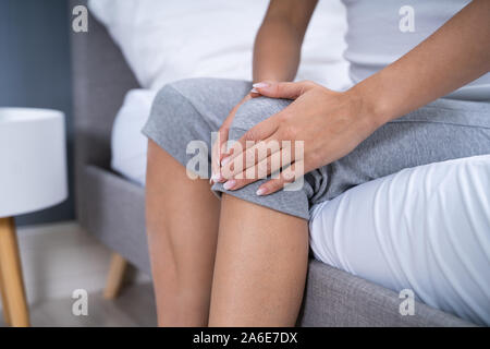 Woman Suffering From Knee Pain Sitting In Bed Stock Photo