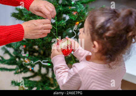 Merry Christmas and Happy Holidays. Grandmother and grandchild decorate the Christmas tree with baubles indoors. The morning before Xmas. Portrait loving family close up. Selective focus. Stock Photo