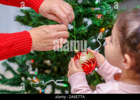 Merry Christmas and Happy Holidays. Grandmother and grandchild decorate the Christmas tree with baubles indoors. The morning before Xmas. Portrait loving family close up. Selective focus. Stock Photo
