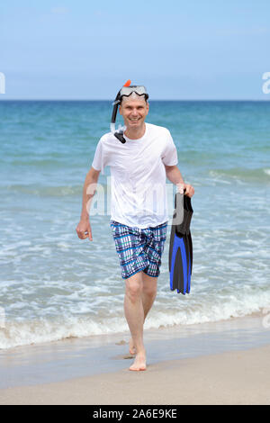 Man with mask, flippers, and snorkel on a sandy beach against a sea Stock Photo