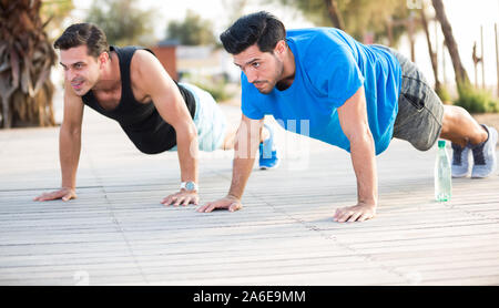 Smiling adult men are doing push-ups in the park. Stock Photo