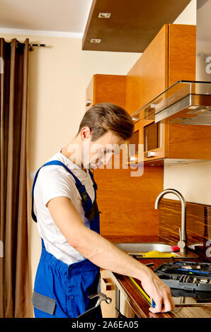 Handyman assembling furniture in kitchen. Man in uniform working as janitor. Stock Photo