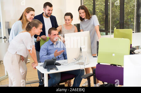 Happy young business men and females talking about new project around computer monitor Stock Photo