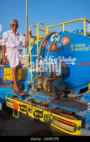 A man in Mangalore, Karnataka, India, standing on his colorfully painted water tanker Stock Photo