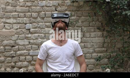 A man watches 360 degree video virtual reality using wearable head mounted display. The movie takes place in all directions and the beholder fills immersed in the scene Stock Photo