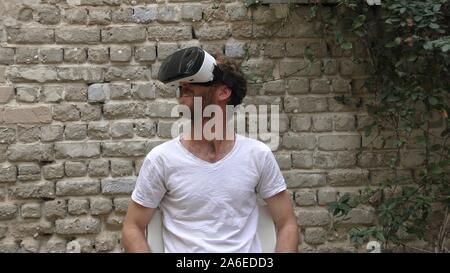 A man watches 360 degree video virtual reality using wearable head mounted display. The movie takes place in all directions and the beholder fills immersed in the scene Stock Photo