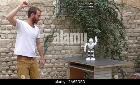 A humanoid robot teaches a young man to dance. The man sees the robot via head mounted display. The robot has a lot of patience and it repeats the same movements precisely. Stock Photo