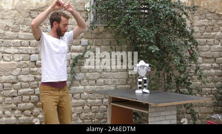 A humanoid robot teaches a young man to dance. The man sees the robot via head mounted display. The robot has a lot of patience and it repeats the same movements precisely. Stock Photo