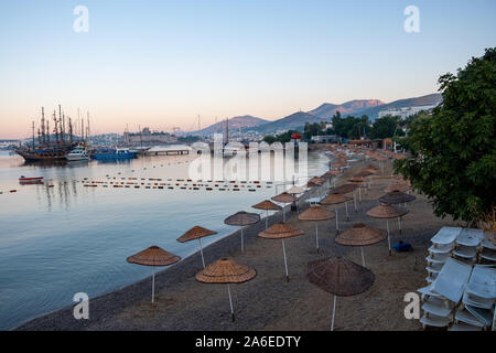 Beautiful view of the empty beach with umbrellas on the background of sunrise over the sea. Turkey, Bodrum, Stock Photo