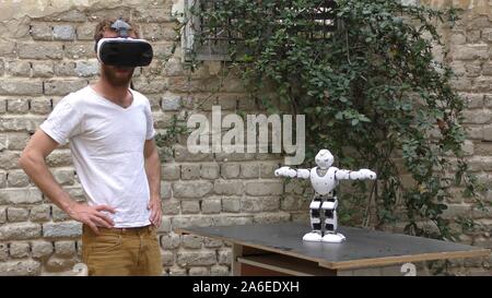 A humanoid robot teaches a young man to dance. The man sees the robot via head mounted display. The robot has a lot of patience and it repeats the same movements precisely. Stock Photo