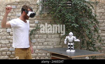 A humanoid robot teaches a young man to dance. The man sees the robot via head mounted display. The robot has a lot of patience and it repeats the same movements precisely. Stock Photo