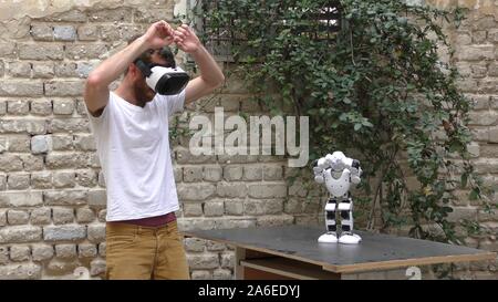 A humanoid robot teaches a young man to dance. The man sees the robot via head mounted display. The robot has a lot of patience and it repeats the same movements precisely. Stock Photo