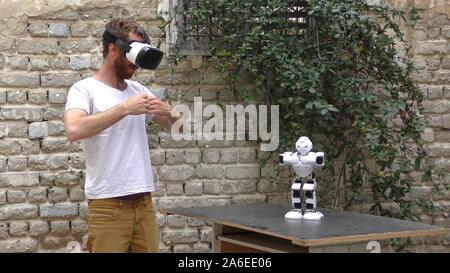 A humanoid robot teaches a young man to dance. The man sees the robot via head mounted display. The robot has a lot of patience and it repeats the same movements precisely. Stock Photo