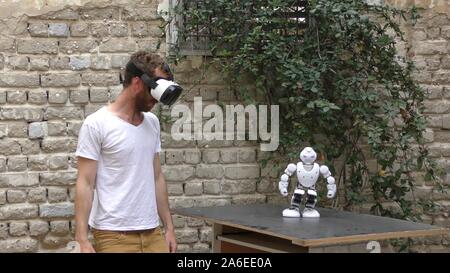 A humanoid robot teaches a young man to dance. The man sees the robot via head mounted display. The robot has a lot of patience and it repeats the same movements precisely. Stock Photo