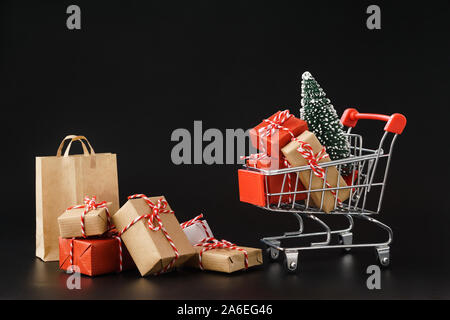 Shopping cart full of various gift boxes and a Christmas tree on black background. Christmas or Black Friday sale concept.