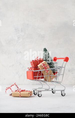 Shopping cart full of various gift boxes and a Christmas tree on light gray background. Christmas sale concept.